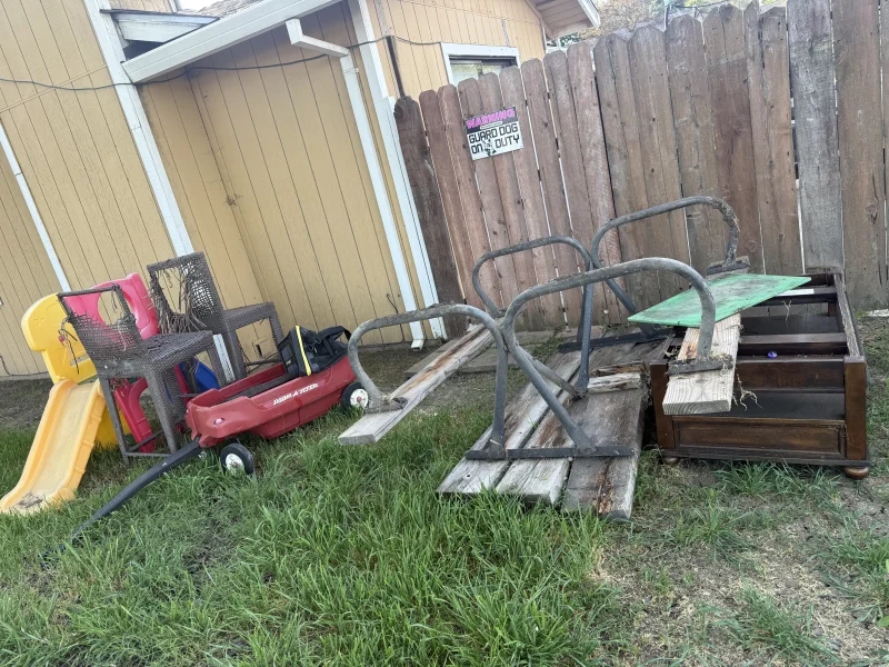 Backyard junk pile with old furniture kids slide and metal frames before removal in Stockton