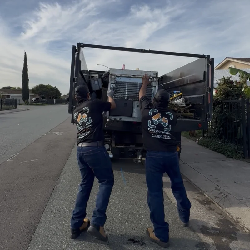 Two ScanJunk crew members loading large appliance into junk removal truck
