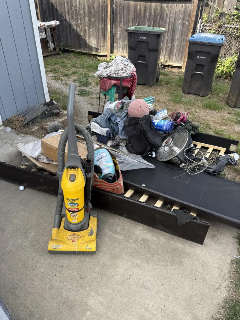 Household junk pile with vacuum cleaner bed frame and miscellaneous items before removal